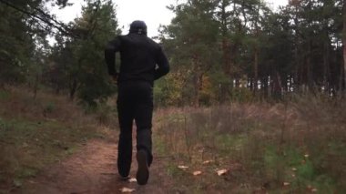 Siyah elbiseli bir adam antrenman yapıyor, çam ağaçları arasında koşuyor, sonbahar.