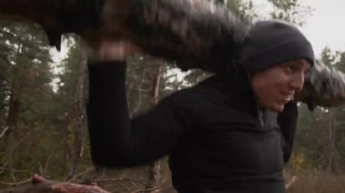 Kaslı sporcu ağır yük kaldırıyor, ormanda kütük tutuyor. Sonbaharda