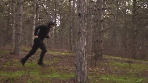 검은 옷을 입은 남자가 나무 사이로 뛰어가서 통나무 위를 뛰어 넘는다 — 비디오