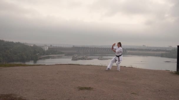 Fordítás: Kyokushinkai. A lány eljegyezte a karate jógát. Természet, gát, város, folyó, erdő, sziklák háttér — Stock videók