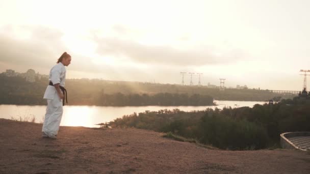 Fordítás: Kyokushinkai. lány kimano karate edzés, edzés, rúgás, nem működik. Folyó, templom, fák háttér — Stock videók