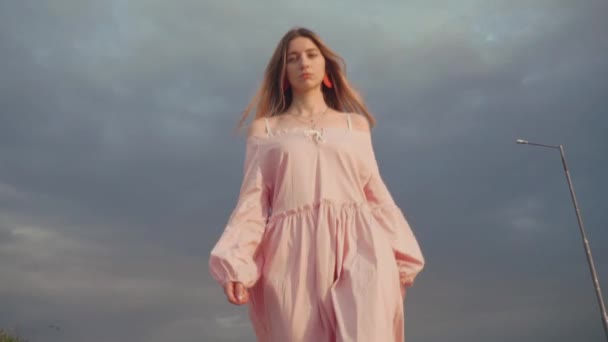Beautiful model in dress walking towards camera, dark, cloudy sky on background — Stock Video