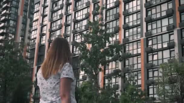 Een zwanger meisje loopt in de zomer in de buurt van een nieuw huis met meerdere verdiepingen — Stockvideo