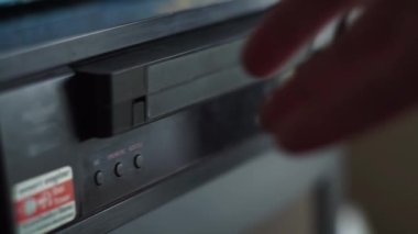 Bir adam video kaseti video oynatıcıya yerleştiriyor. Elle yakından çek. Siyah video eski bir televizyonun yanında.