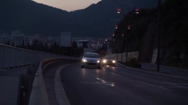 Дорога, вид на рухливі автомобілі вздовж схилу, сутінки, вогні, фари ввімкнені, за горою — стокове відео