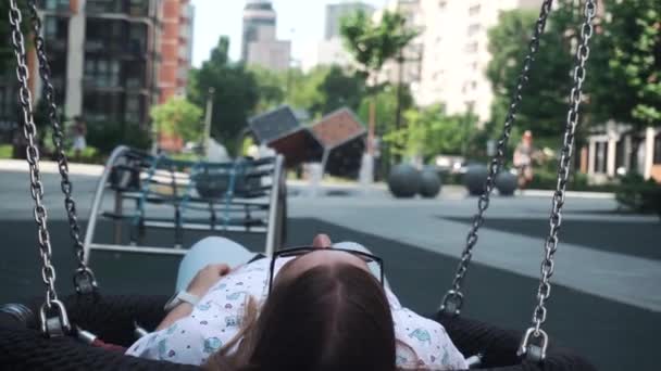 Dívka s tmavými vlasy pomalu válcování houpačka uvolněný odpočinek přední hřiště, fontány — Stock video