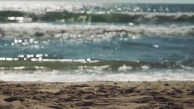 Büyük köpüklü dalgalar kıyıya vurur, güneş ışınları berrak suya yansır.