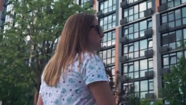 Zwangere jonge vrouw loopt langs een nieuw flatgebouw. groene bomen achtergrond — Stockvideo
