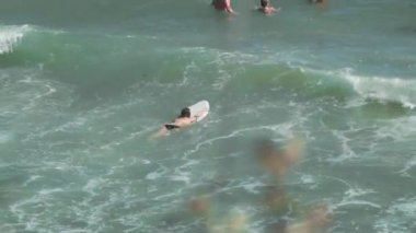 Sörf tahtası olan bir kız denize doğru koşar, büyük dalgaları yakalar ve yere yuvarlanır.