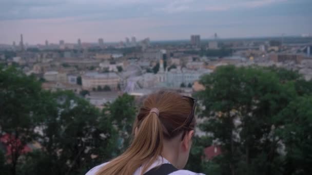 Chica con el pelo rojo se para con su espalda contra el fondo de la ciudad — Vídeos de Stock