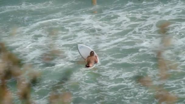 Meisje met surfplank loopt verder in zee, vangt grote golf en rolt liggend — Stockvideo