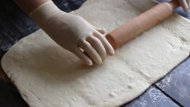 Handen in handschoenen rol het deeg uit op een houten ondergrond. Koken. Bakkerijproducten. — Stockvideo
