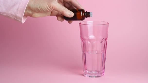 Oudere vrouwen hand giet medicijnen in een glas water op een roze achtergrond. Geneeskunde. Ziekte. — Stockvideo