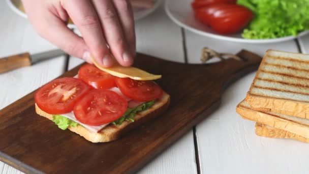 샐러드, 토마토, 햄, 치즈와 함께 샌드위치를 만드는 과정입니다. 미국 요리. 패스트 푸드. 요리. — 비디오