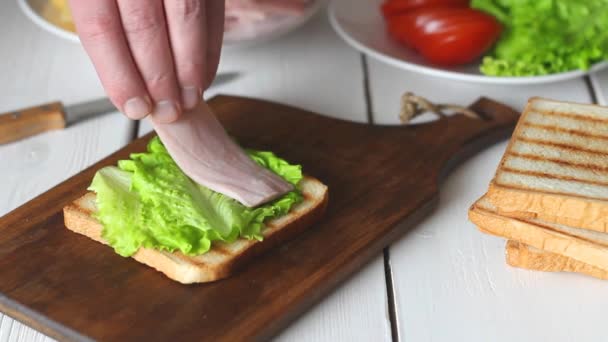 Het maken van een sandwich met salade, tomaat, ham en kaas. Amerikaanse keuken. Fast food. Koken. — Stockvideo