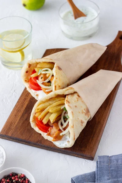 Greek dish gyros with chicken, french fries, tomatoes, onions and pita. Greek cuisine