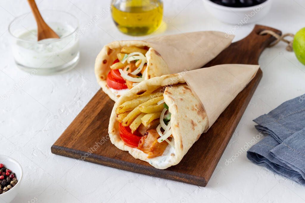 Greek dish gyros with chicken, french fries, tomatoes, onions and pita. Greek cuisine