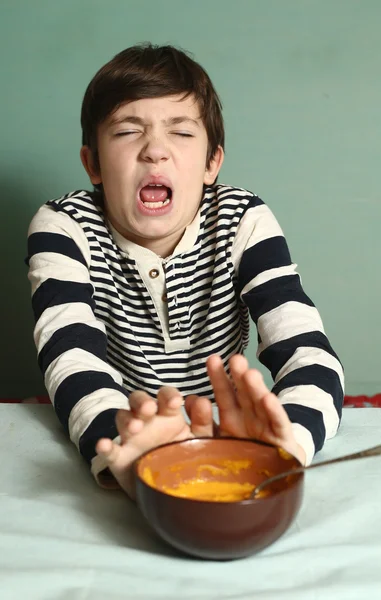 Niño comer sopa de calabaza con expresión de disgusto —  Fotos de Stock