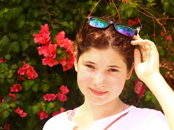 Chica en gafas de sol en flores rojas arbusto fondo — Foto de Stock