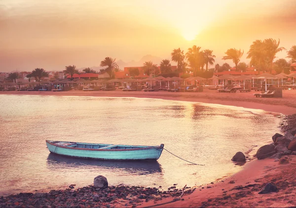 Захід сонця на пляжі з самотнім синім човном — стокове фото