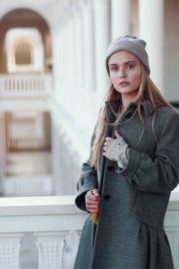  Akçaağaç yapraklı örgü şapkalı ve ceketli sarışın kız. Şehir mimarisinin arka planında portreyi kapat.