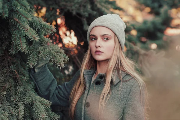 Blond girl in knitted hat and coat close up portrait on on blue spruce background — Stock Photo, Image