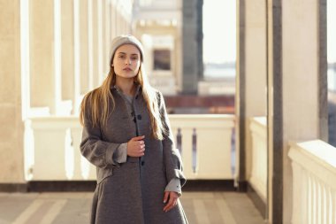  Akçaağaç yapraklı örgü şapkalı ve ceketli sarışın kız. Şehir mimarisinin arka planında portreyi kapat.