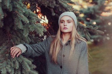  Örgü şapkalı ve ceketli sarışın kız mavi ladin arka planında yakın plan portresi