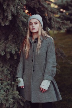  Örgü şapkalı ve ceketli sarışın kız mavi ladin arka planında yakın plan portresi