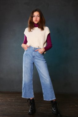 Kot çizmeli genç kız yelek ördü mavi duvar arkasına vücut portresi ördü