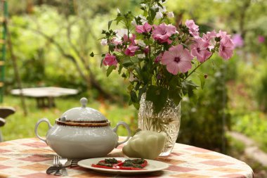 Kırsal kesimde hala hayat var. Kaseler, pastalar, pesto soslu patates püresi ve domates. Masada çiçek buketi, yeşil bahçe arka planında yakın plan fotoğrafı.