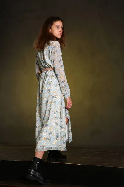 model girl in long printed dress and black boots full body portrait walking on dark wall background