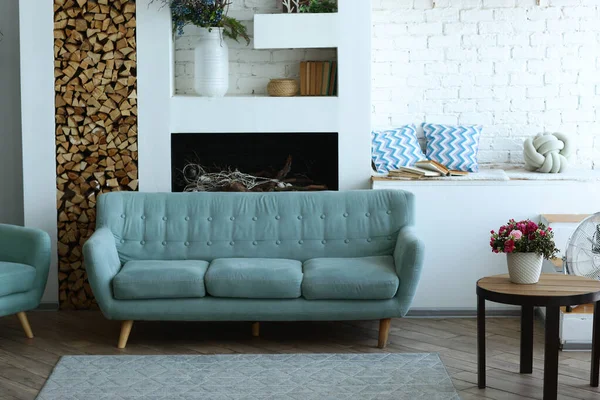 Roztomilý moderní ložnicový interiér s modrou pohovkou, krbem, květináčem, kobercem a stolem — Stock fotografie