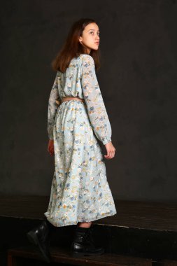 Uzun baskılı elbisesi ve siyah botları olan model bir kız. Arka planda yürüyen siyah bir vücut portresi.