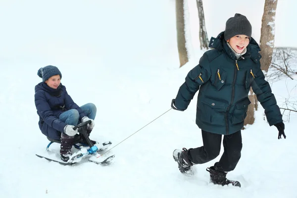 Siblings boy and girl ride snow scooter on winter white backgrou — Stockfoto