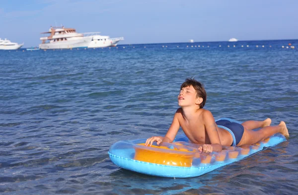 Schöner Junge im Badeanzug mit aufblasbarer Matratze auf dem blu — Stockfoto