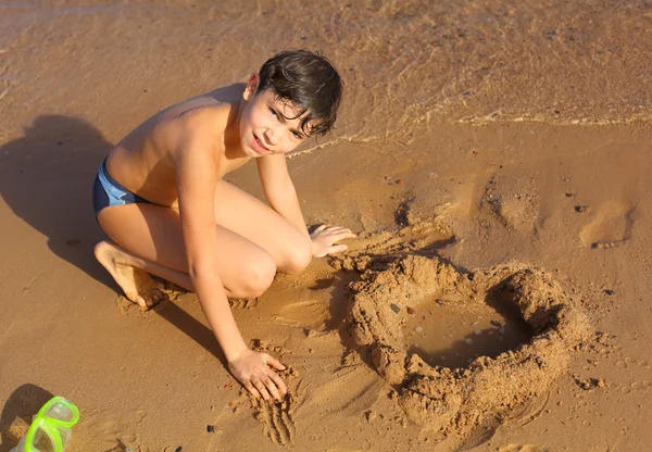 Preteen bel ragazzo scultura sabbia cuore sulla spiaggia del mare rosso — Foto Stock