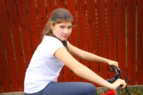 Vacker tonårsflicka rida cykel på bruna staketet bakgrunden — Stockfoto