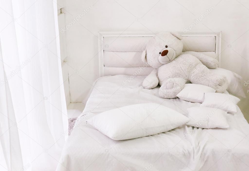white room corner with bed teddy bear and window with white curt