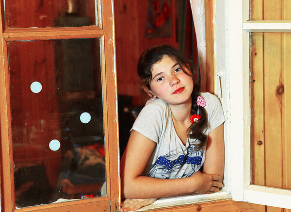 preteen beautiful girl with plait look out of the wooden window