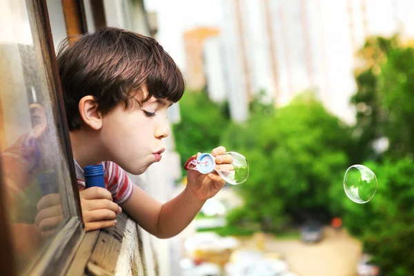 Preteen schöner Junge mit Seifenblasen lood aus dem Fenster — Stockfoto