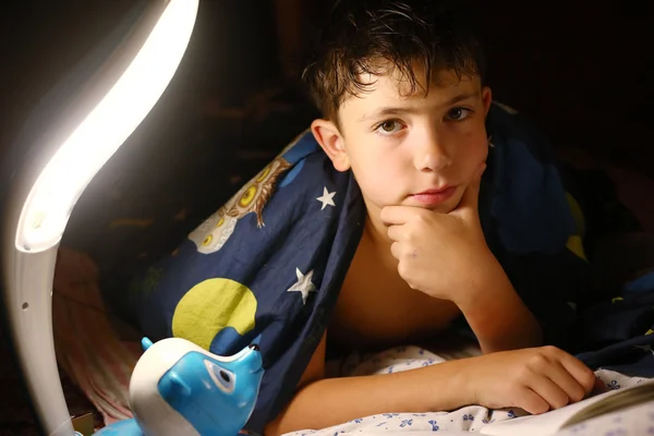 Nedospělý hezký kluk četl knihu s lampou před spaním — Stock fotografie