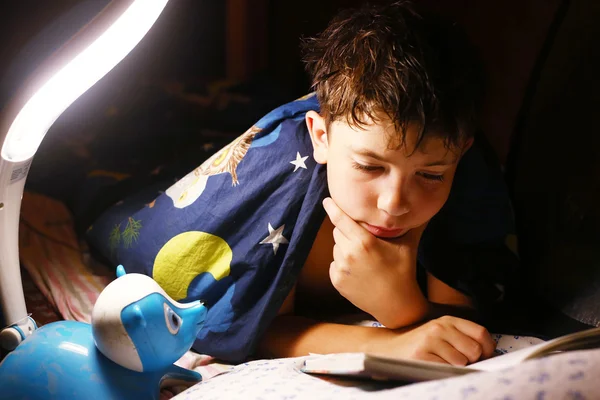 Preteen bonito menino ler livro com lâmpada antes de dormir — Fotografia de Stock