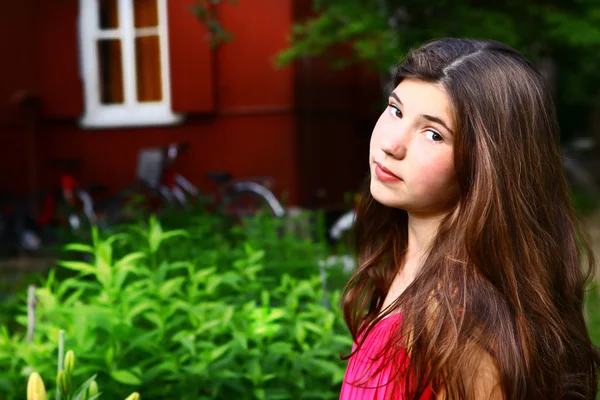 Bela menina adolescente com longos cabelos castanhos grossos fechar-se retrato no país casa de campo de verão e jardim de fundo — Fotografia de Stock