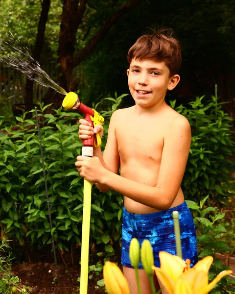 Preteen όμορφο αγόρι με πότισμα σωλήνα το πράσινο φόντο είναι κήπων — Φωτογραφία Αρχείου
