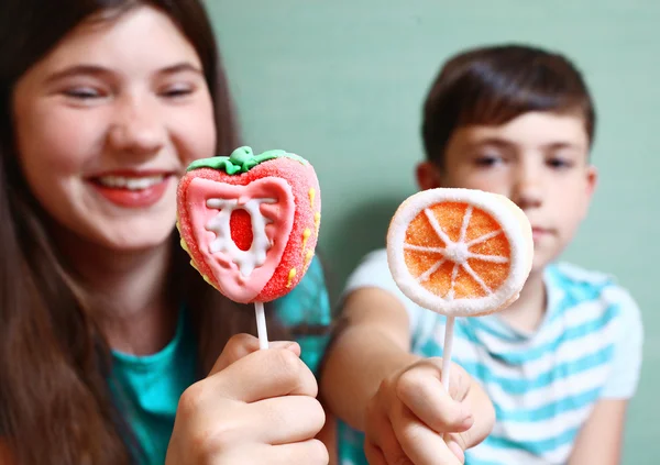 フルーツ オレンジ、幸せな子供女の子と背景の男の子を笑顔でイチゴとして設計されたスティック上の 2 つのマシュマロ キャンデー — ストック写真