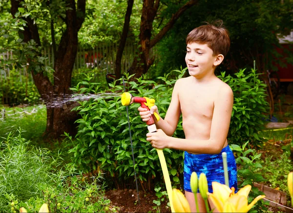 Menino com tubo de rega no fundo do jardim verde — Fotografia de Stock