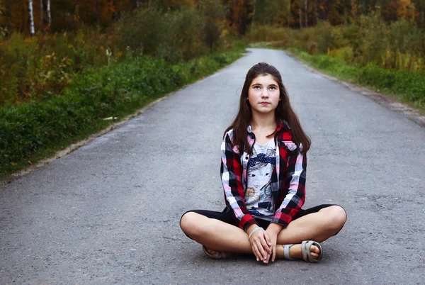 Bela adolescente menina sentar-se no campo vazio estrada — Fotografia de Stock