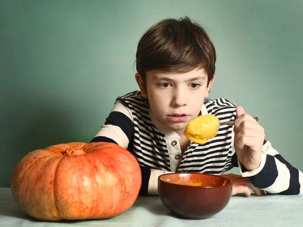 Menino com grande abóbora laranja comer purê de sopa de creme — Fotografia de Stock