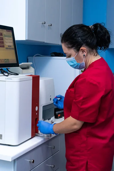 Nurse introducing a sample of blood serum for analysis in a biochemistry machine